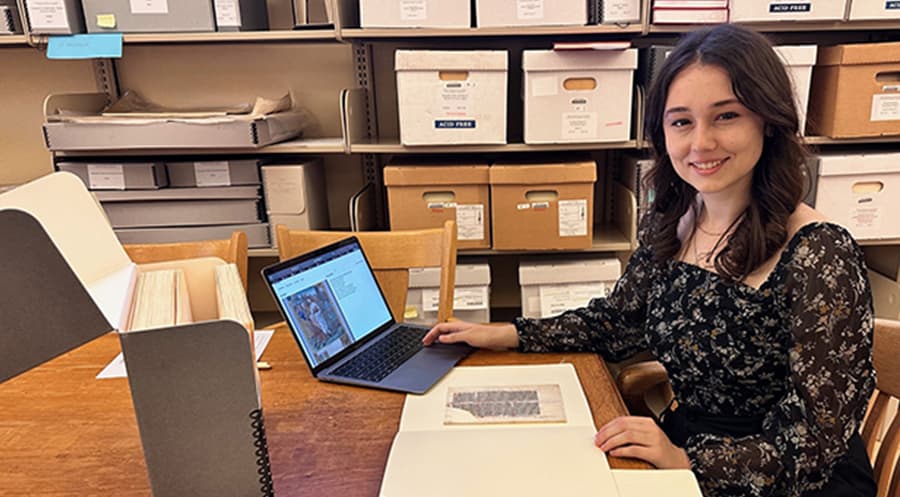 Kaitlynn Norton seated at a table with a manuscript and laptop.