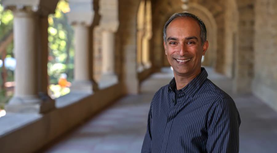 Vijoy Abraham standing in a colonnade smiling at the camera.