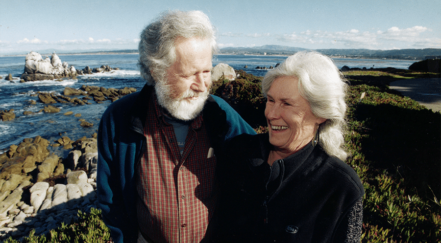 A smiling couple standing on the shoreline of the Monterey Bay.