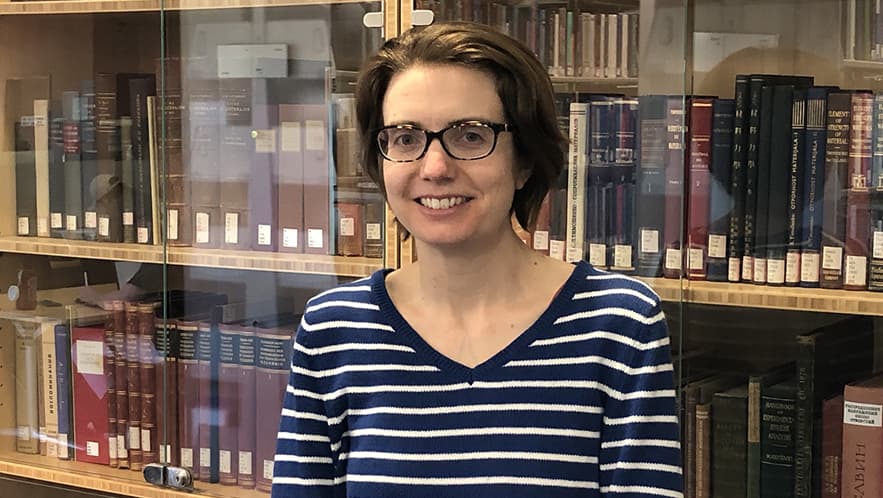 Linnea Shieh, Head of Terman Engineering Library standing in front of a glass enclosed book case.