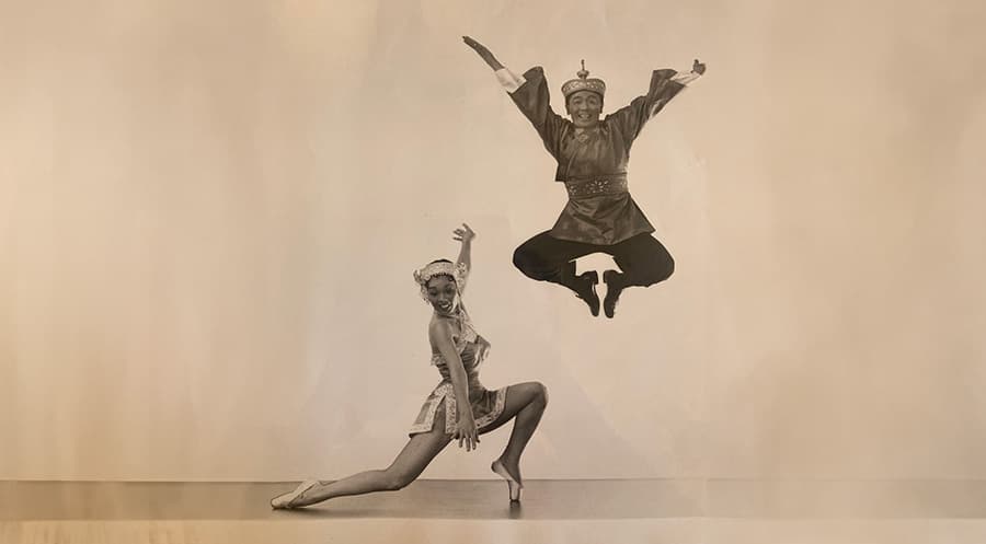 Dorothy Toy and Paul Wing posing, Paul jumping up in the air with his feet together and Dorothy lunging on the ground with one foot on point.